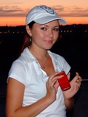 Image showing The young girl with a red thin mobile phone in hands