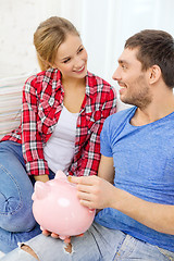 Image showing smiling couple with piggybank sitting on sofa