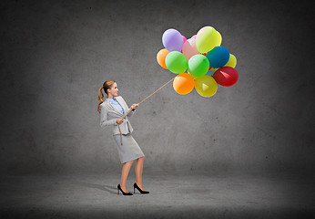 Image showing smiling businesswoman pulling rope with balloons