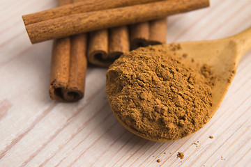 Image showing Cinnamon, whole sticks behind wooden spoon with a heap of powder