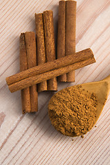 Image showing Cinnamon, whole sticks behind wooden spoon with a heap of powder