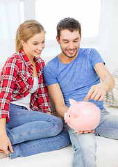 Image showing smiling couple with piggybank sitting on sofa