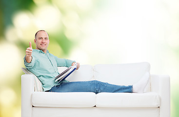 Image showing smiling man lying on sofa with book