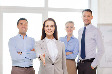 Image showing smiling businesswoman in office with team on back