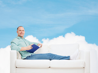 Image showing smiling man lying on sofa with book