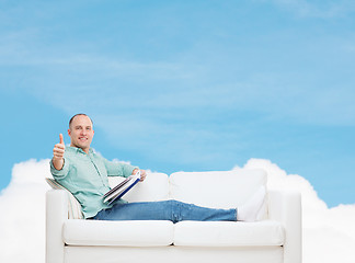 Image showing smiling man lying on sofa with book