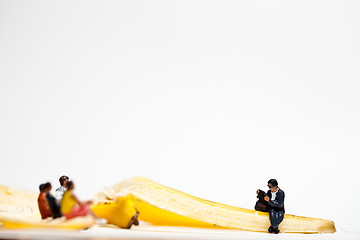 Image showing Miniature people in action stting on a banan