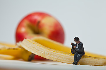 Image showing Miniature people in action stting on a banan