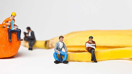 Image showing Miniature people in action stting on a banan