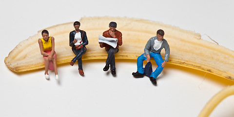 Image showing Miniature people in action stting on a banan