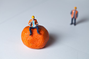 Image showing Miniature people in action and man sitting on an orange