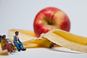 Image showing Miniature people in action stting on a banan