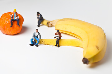 Image showing Miniature people in action stting on a banan