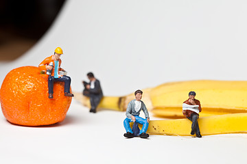 Image showing Miniature people in action stting on a banan