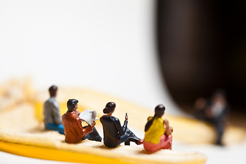 Image showing Miniature people in action stting on a banan