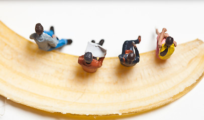 Image showing Miniature people in action stting on a banan