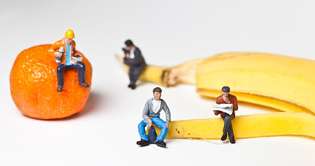 Image showing Miniature people in action stting on a banan