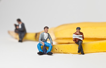 Image showing Miniature people in action stting on a banan