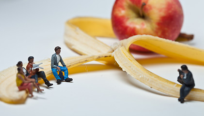 Image showing Miniature people in action stting on a banan