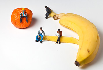 Image showing Miniature people in action stting on a banan