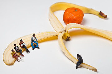 Image showing Miniature people in action stting on a banan