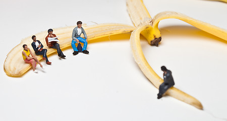 Image showing Miniature people in action stting on a banan