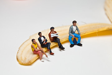 Image showing Miniature people in action stting on a banan