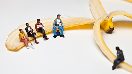 Image showing Miniature people in action stting on a banan