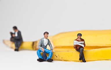 Image showing Miniature people in action stting on a banan