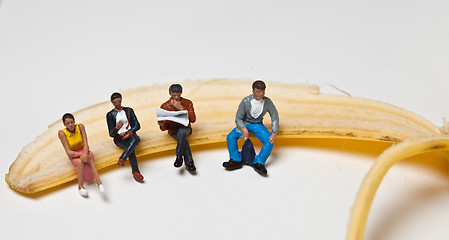 Image showing Miniature people in action stting on a banan