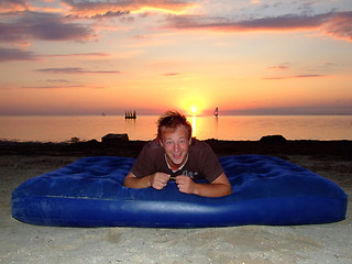 Image showing The joyful guy on a mattress on a background of a sunset