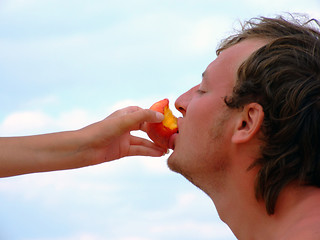 Image showing The female hand feeds the guy with a peach