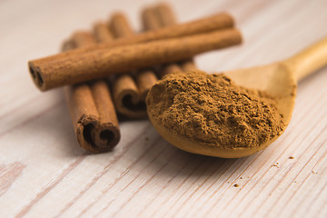 Image showing Cinnamon, whole sticks behind wooden spoon with a heap of powder