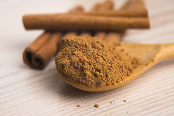 Image showing Cinnamon, whole sticks behind wooden spoon with a heap of powder