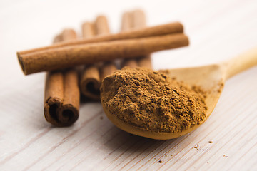 Image showing Cinnamon, whole sticks behind wooden spoon with a heap of powder