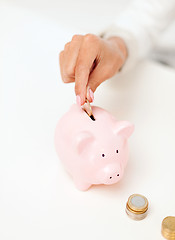 Image showing female hand putting euro coins into piggy bank