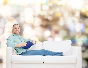 Image showing smiling man lying on sofa with book