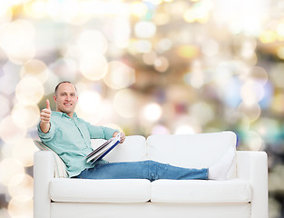 Image showing smiling man lying on sofa with book