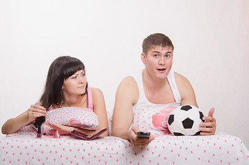 Image showing Girl paints her nails in bed, man emotionally watching soccer