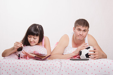 Image showing Girl paints her nails in bed, man emotionally watching soccer