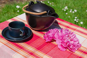 Image showing black ceramic teapot and cup with peony on table  