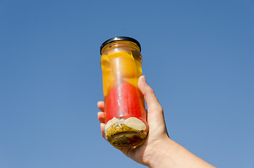 Image showing hand hold marinated pepper  jar on sky background 