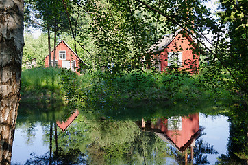 Image showing red rural home reflected through branches on pond 
