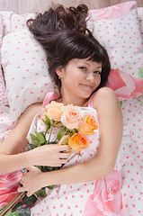 Image showing Beautiful young girl lying in bed with bouquet of roses