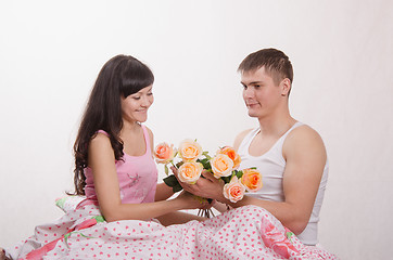 Image showing Girl receives flowers from guy sitting in bed