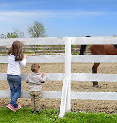 Image showing Pre-teen girl and Baby boy on the a white picket fence beside th