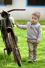 Image showing 2 years old curious Baby boy walking around the old bike 