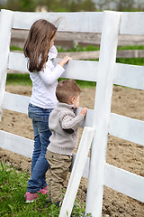 Image showing Pre-teen girl and Baby boy on the a white picket fence beside th