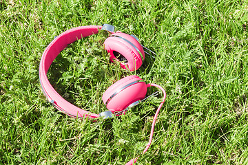 Image showing Bright colored pink headphones on green sward