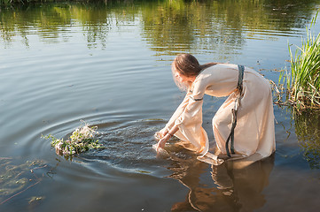 Image showing Beautiful girl lowers wreath in water